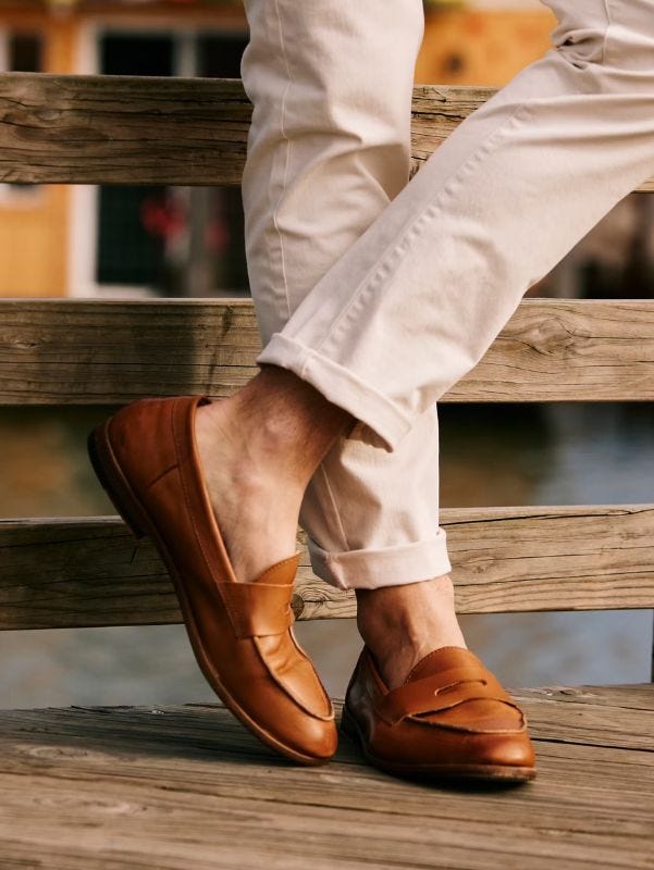 close-up of a man's feet in brown penny loafers one leg crossed over the other