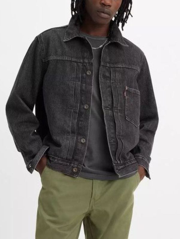 man from the neck down wearing a black denim trucker jacket over a grey shirt with olive green pants