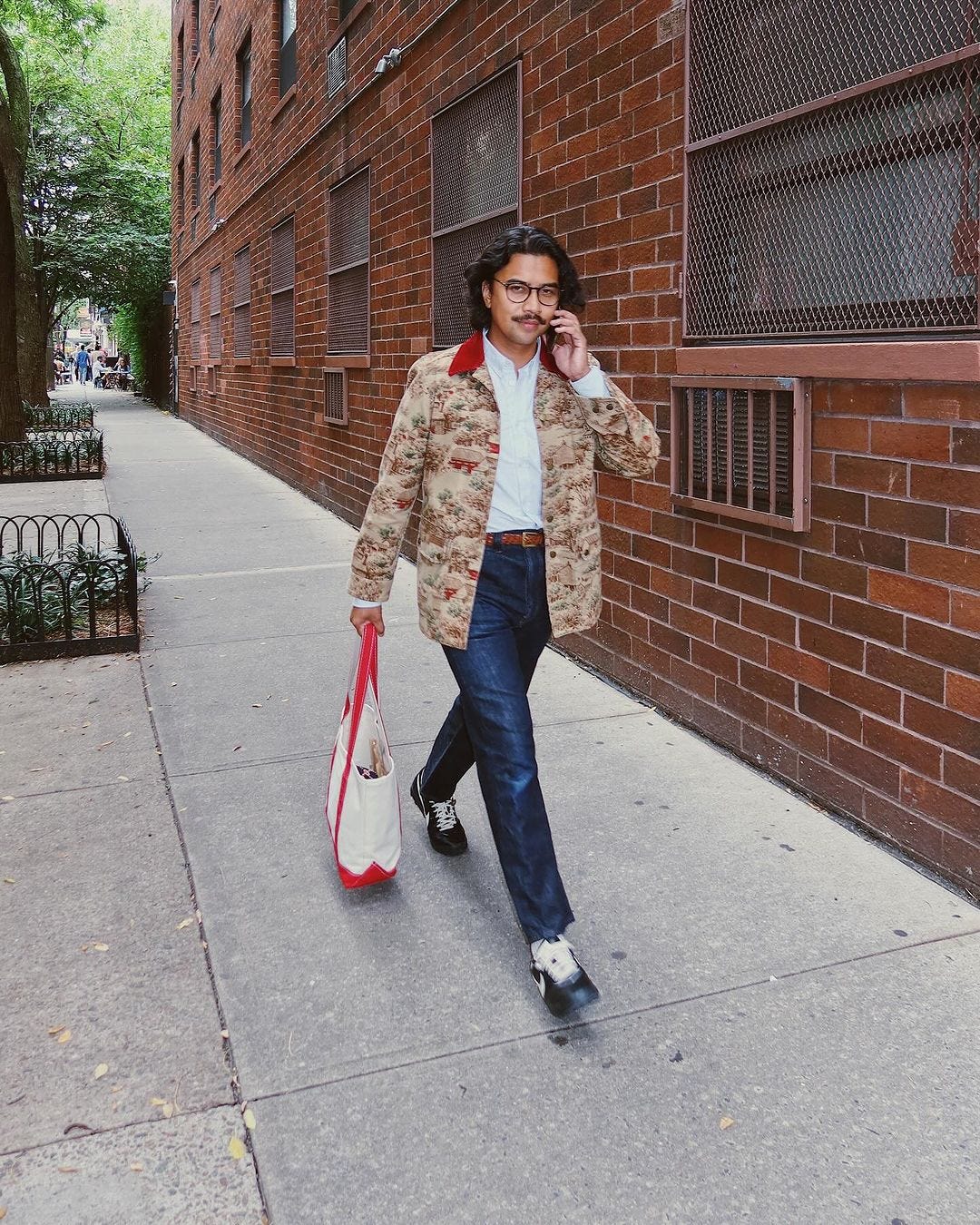 man walking on the street wearing a patterned chore coat with a white button-down shirt and blue jeans