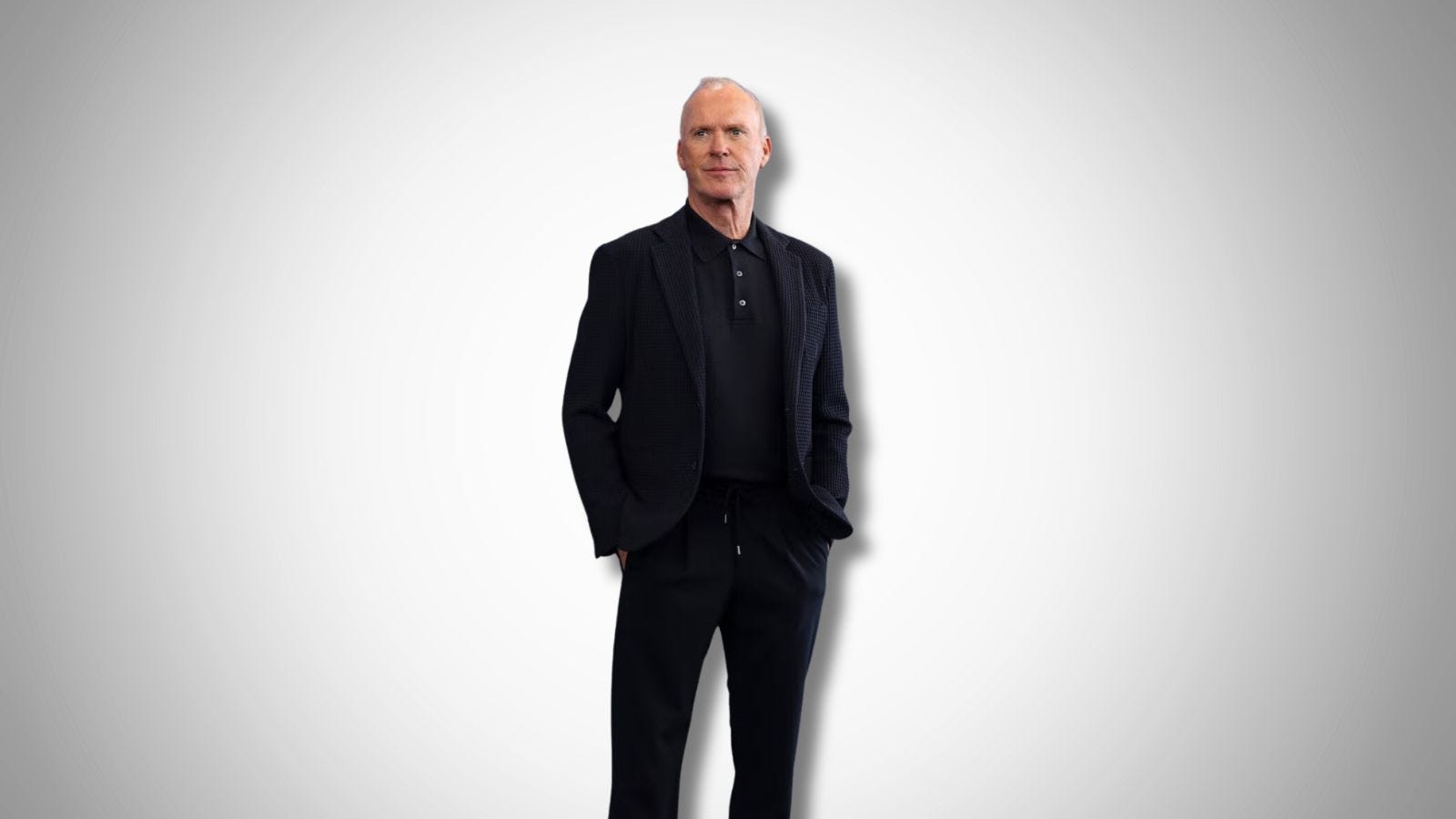 the actor Michael Keaton in a black suit with a black knit polo. his hands are in his pockets