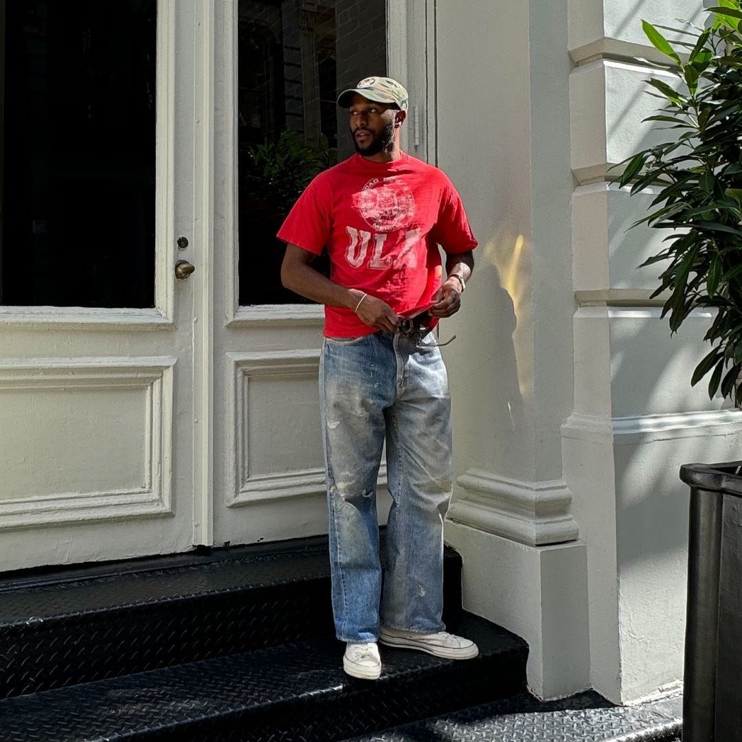 young man standing on a building stoop wearing a red t-shirt with ripped jeans and white converse all star sneakers, converse high top sneaker outfits