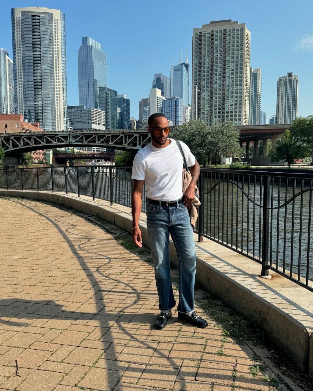 man standing by a river wearing a white t-shirt, blue jeans, and black loafers