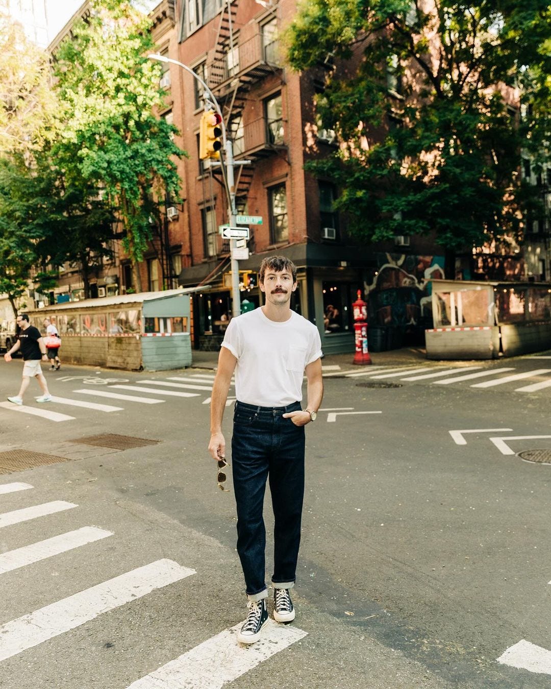 man standing in the street wearing a white t-shirt, dark jeans, and converse chuck taylor sneakers