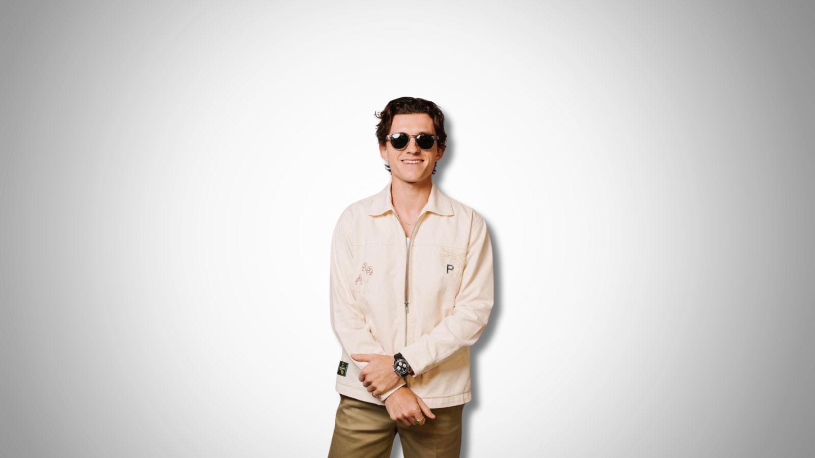 Tom Holland wearing sunglasses, a light jacket and tan chinos