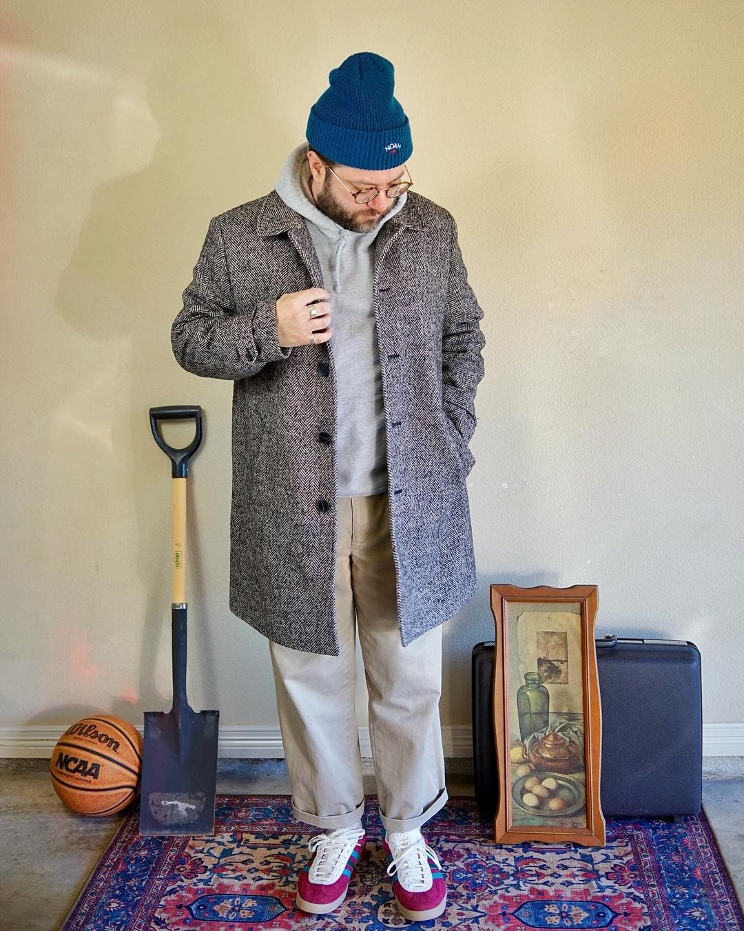 man wearing a blue beanie, textured topcoat, grey hoodie, tan khakis, and red and blue sneakers