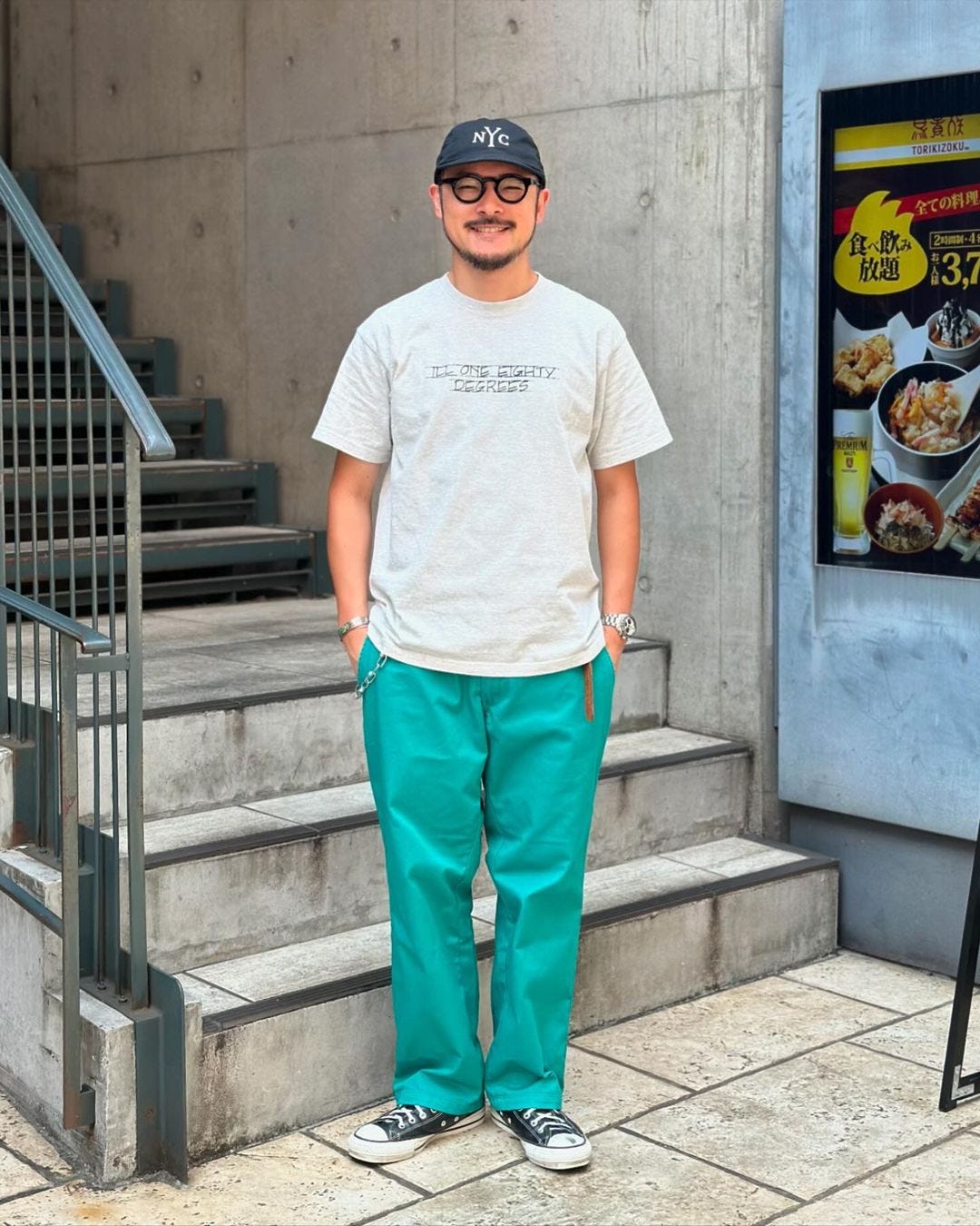 man standing on a staircase wearing a white t-shirt with teal pants and converse chuck taylors