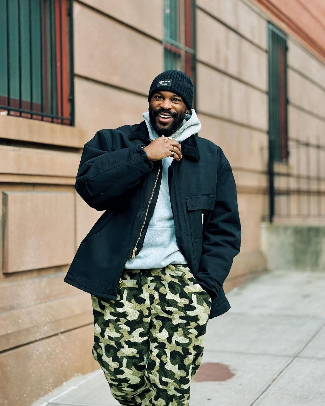 close-up of man wearing black workwear jacket, camo pants and a grey hoodie