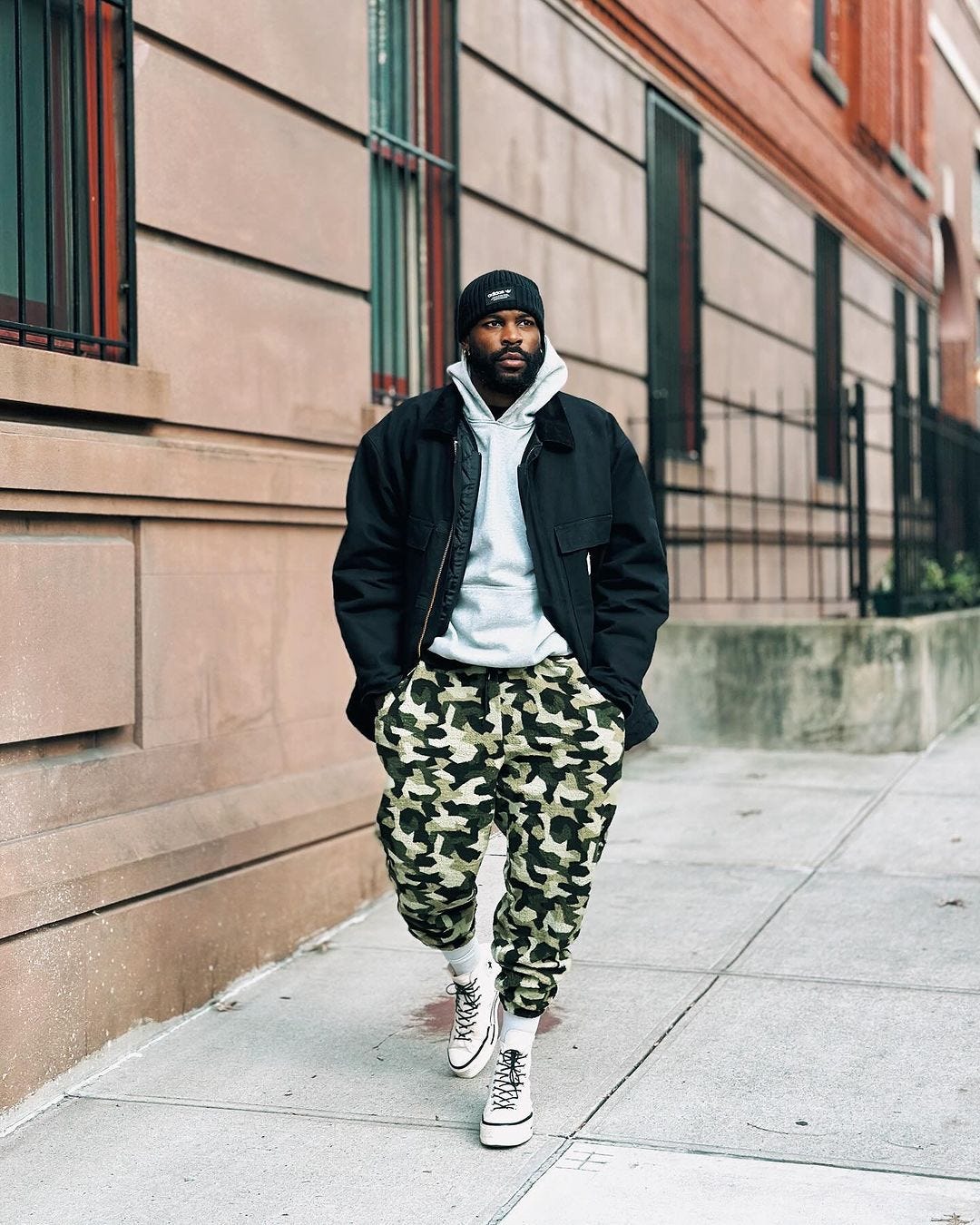 man walking down the street wearing black workwear jacket, camo pants and a grey hoodie