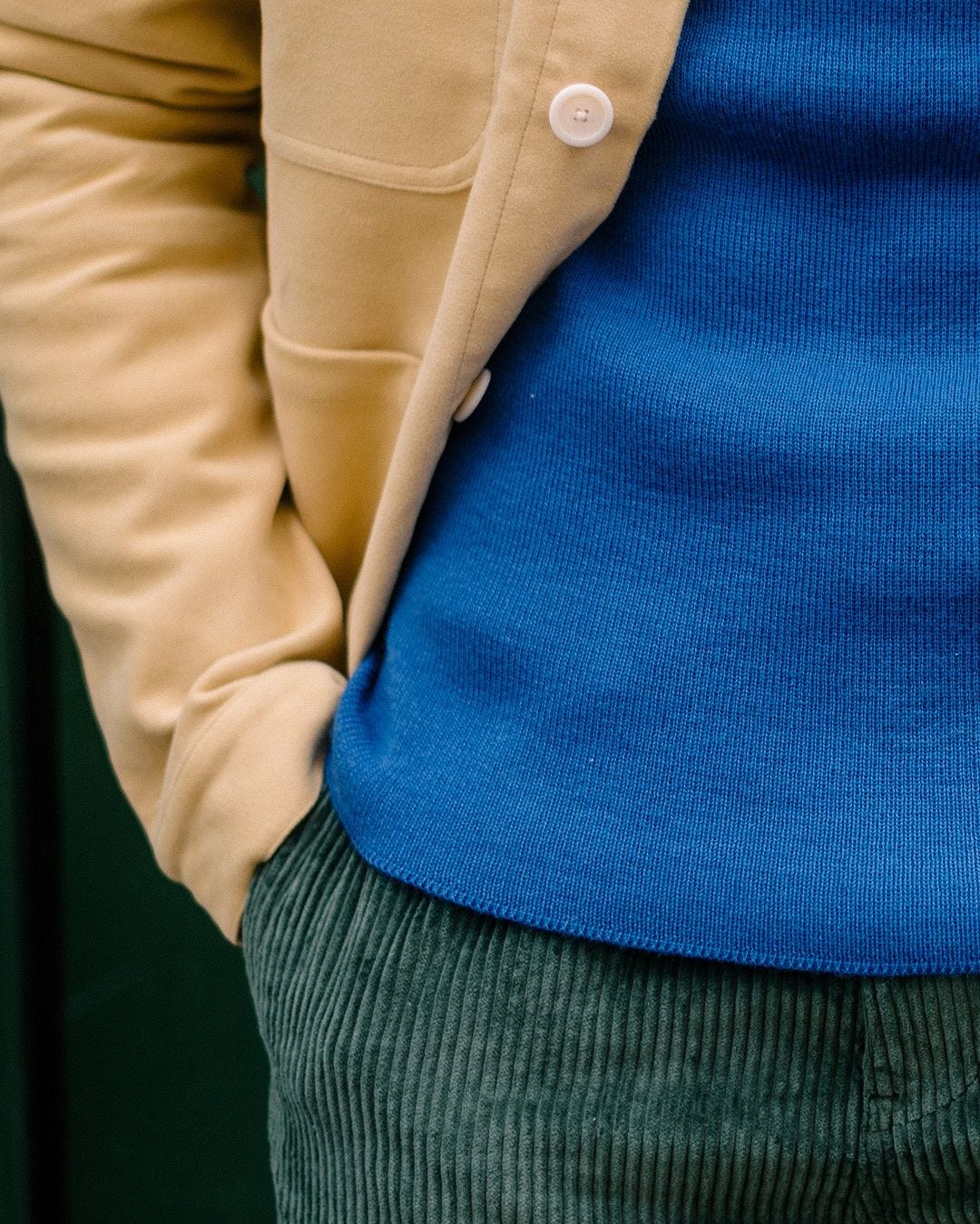 close up of a man wearing a tan chore coat, blue sweater and green corduroy pants