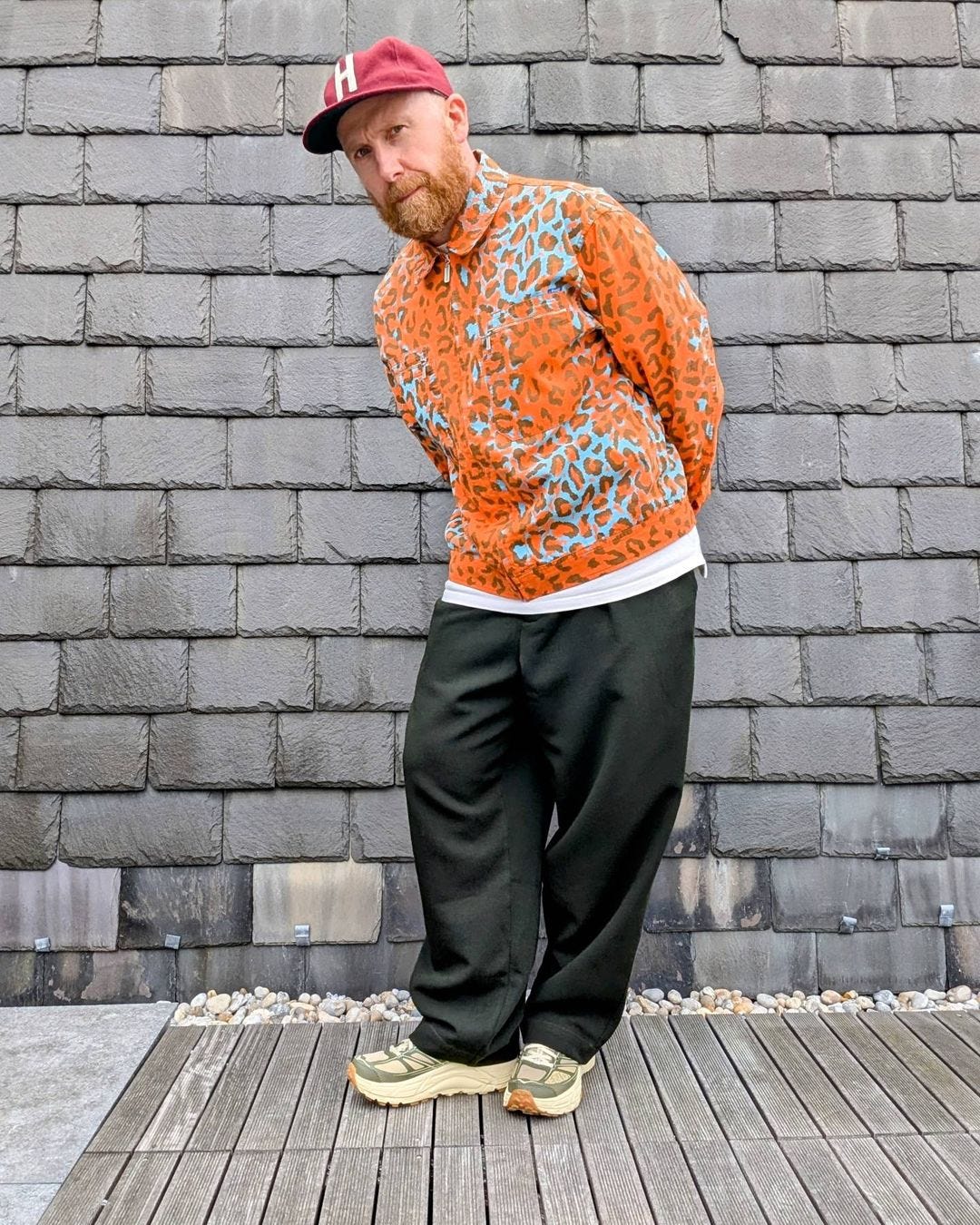 man wearing a bold orange jacket with baggy pants, sneakers, and a baseball hat