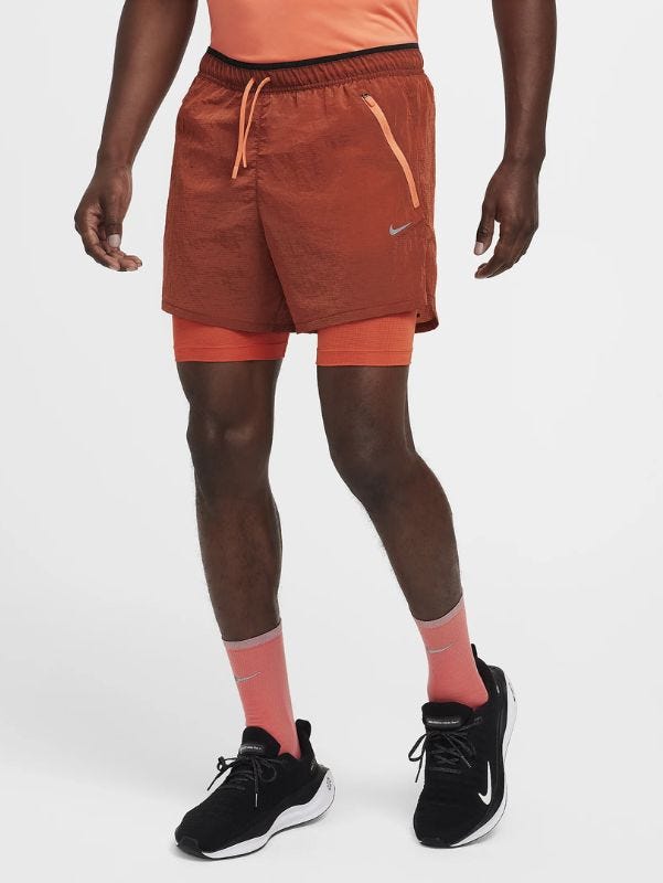 Lower body of man wearing orange running shorts, orange socks and black running sneakers