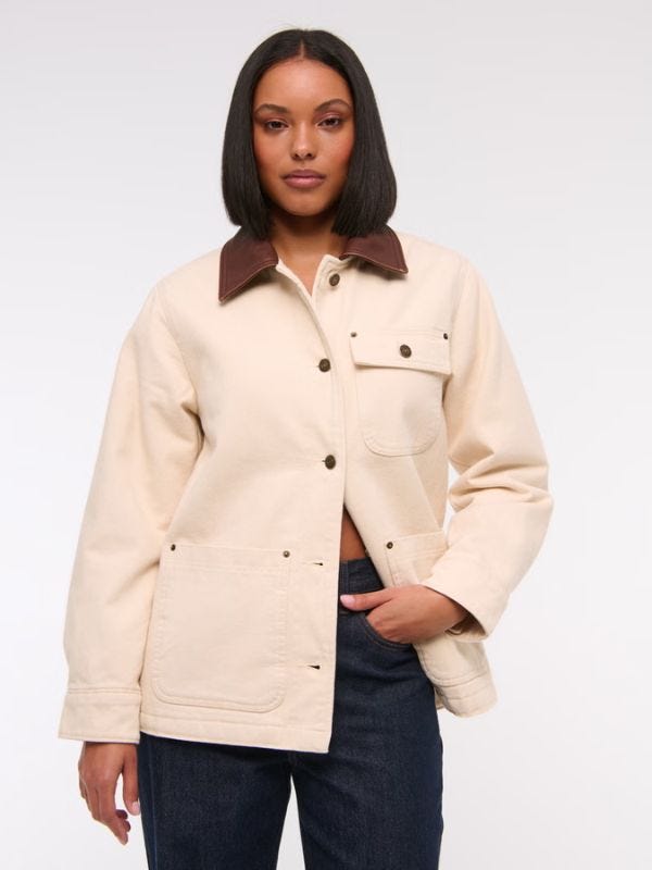 attractive woman wearing a cream-colored workwear jacket with a brown collar and dark buttons