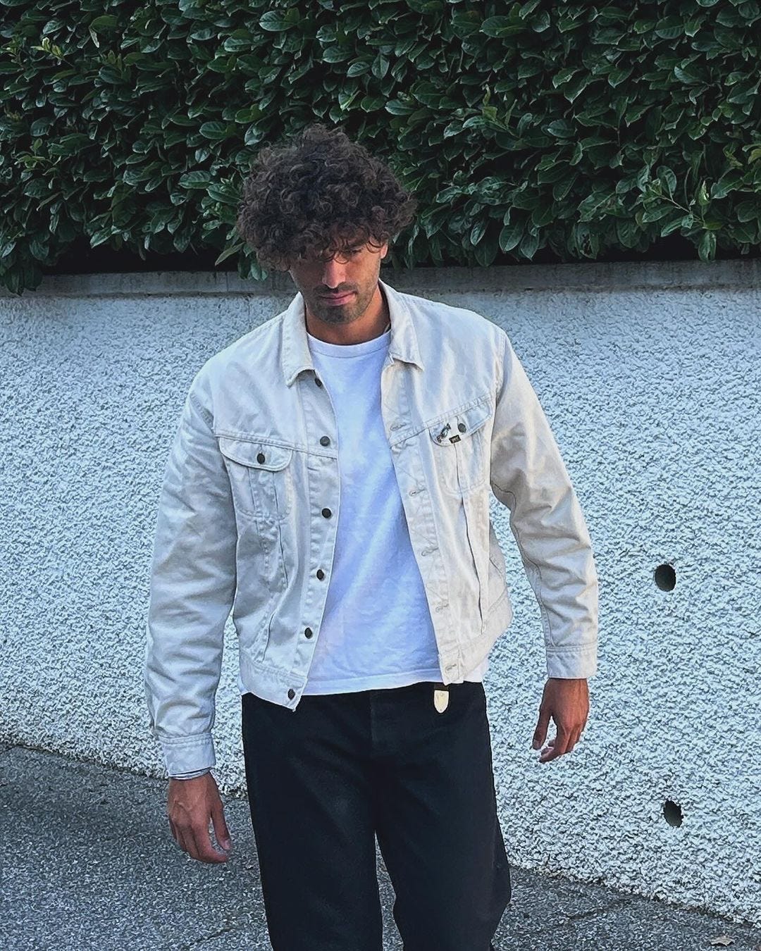 man wearing a white denim jacket over a white t-shirt with black jeans and a western-style black belt