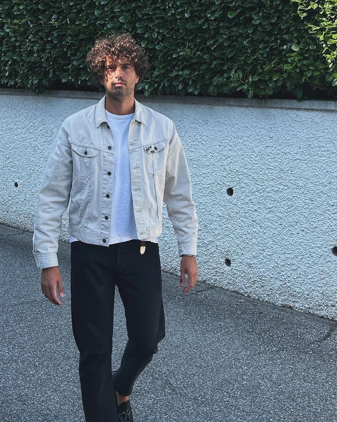 man wearing a white denim jacket over a white t-shirt with black jeans and a western-style black belt with loafers