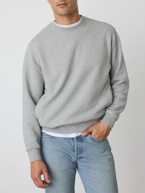 Man wearing gray crew neck sweatshirt, white T-shirt and light blue jeans from neck to waist