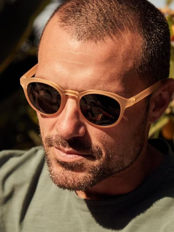 stylish man wearing tan-colored plastic frame sunglasses with dark lenses