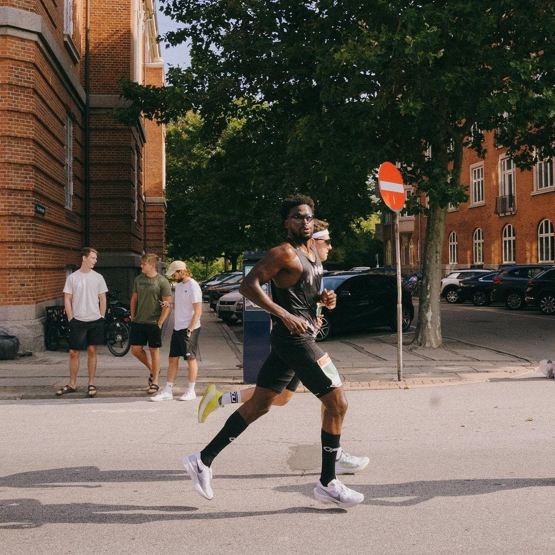 Two athletes running in front of three casually dressed young people during a race across the street