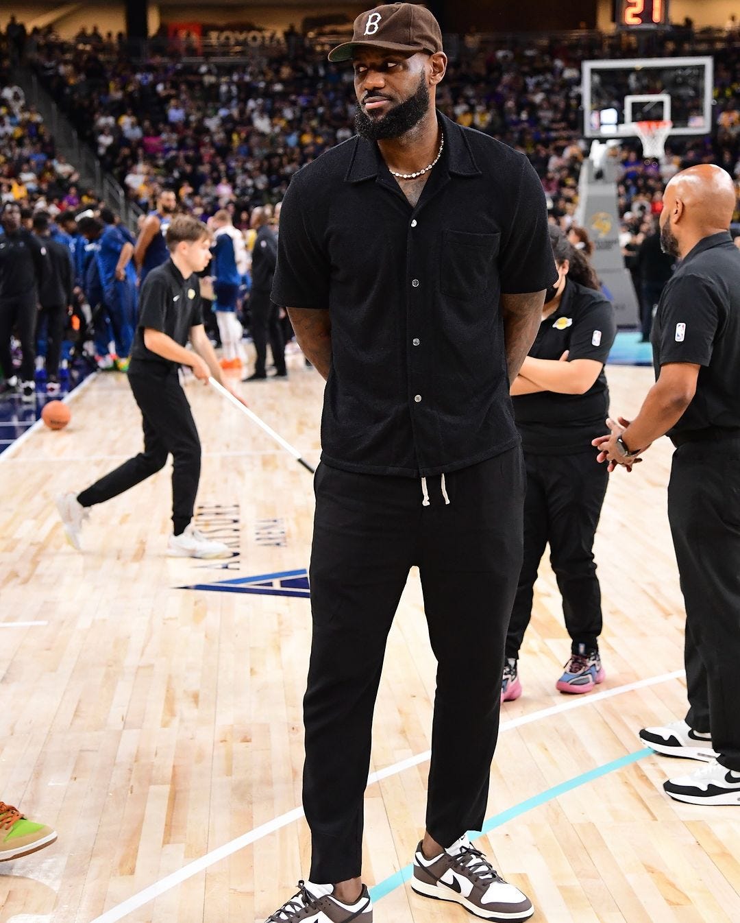 LeBron James wearing a short-sleeve black button down shirt and black drawstring pants at a basketball game