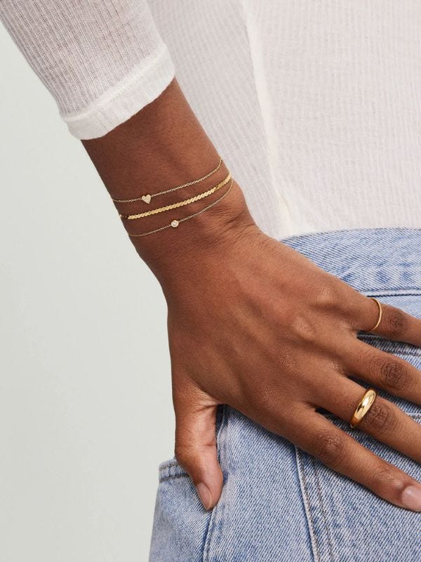 woman's wrist, she is wearing three delicate gold bracelets