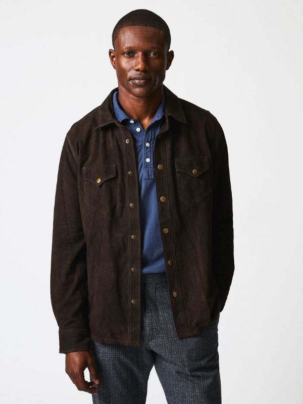 Man wearing brown suede overalls, navy polo shirt and textured trousers from waist up