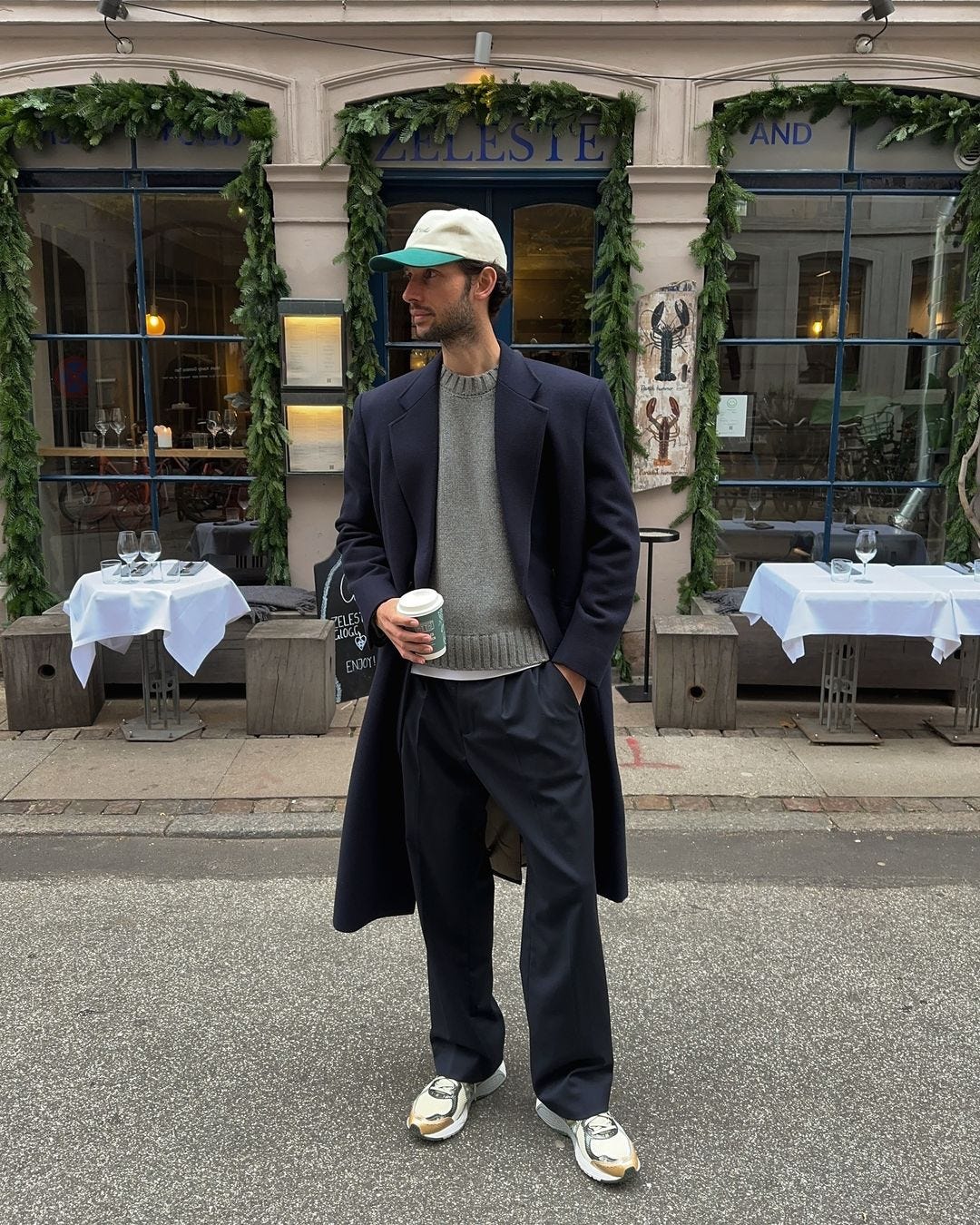 stylish man wearing a navy topcoat over a grey sweater with dark pants and white sneakers