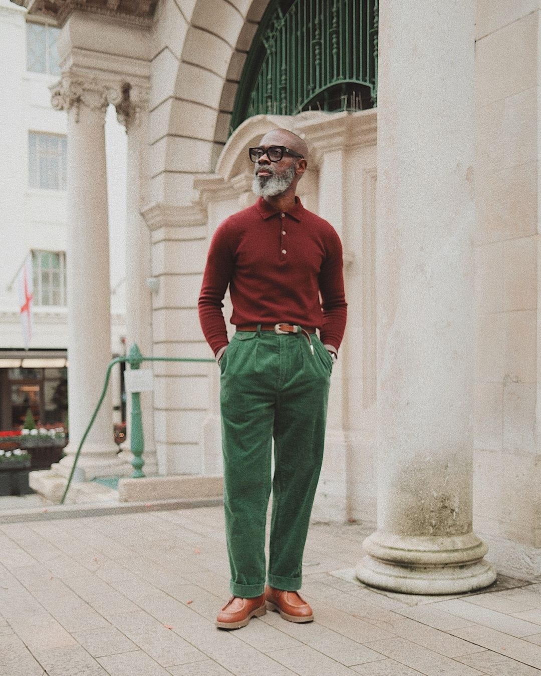 stylish man wearing a burgundy long-sleeve knit polo with green pants and brown lace-up shoes