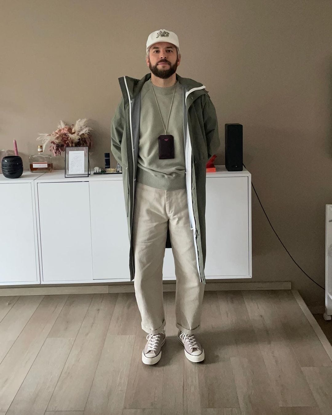 man wearing an olive water-resistant long coat over a light crewneck sweatshirt with chinos and tan sneakers