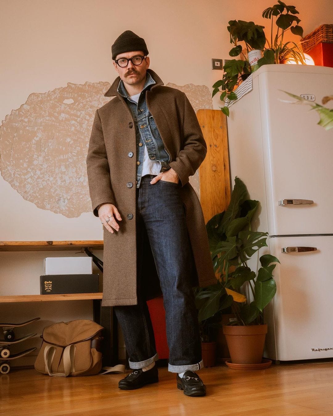 man wearing a brown overcoat over a buttoned denim jacket with a white t-shirt, dark jeans, and black loafers