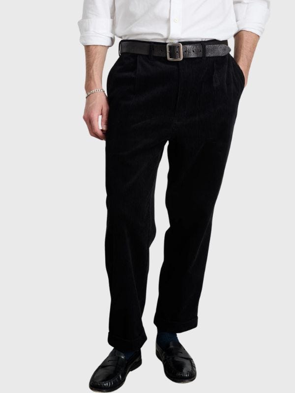 man from the waist down wearing pleated black corduroy trousers with a black belt and whtie button-down shirt