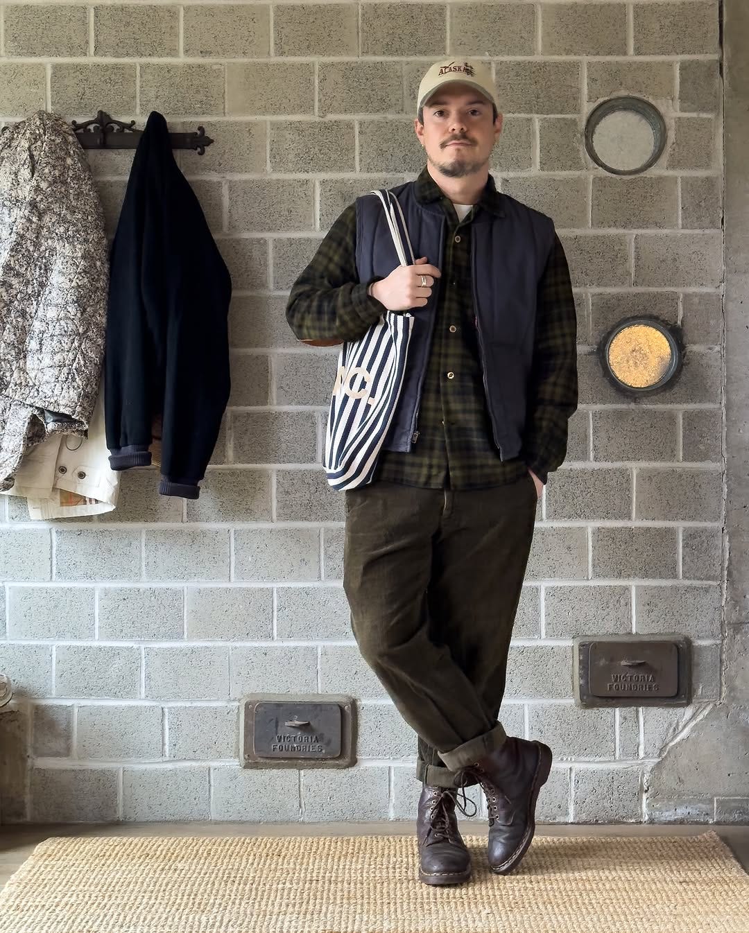 stylish man wearing a plaid shirt and dark corduroy pants with a navy vest and white baseball hat