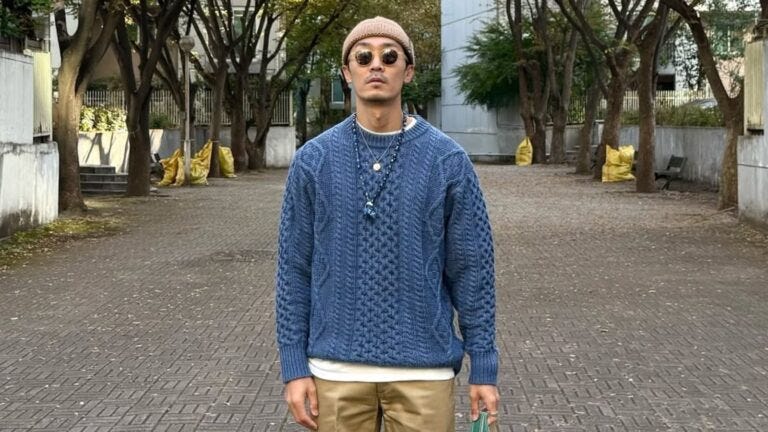 stylish man wearing a beanie, sunglasses, blue fisherman sweater, and tan chinos