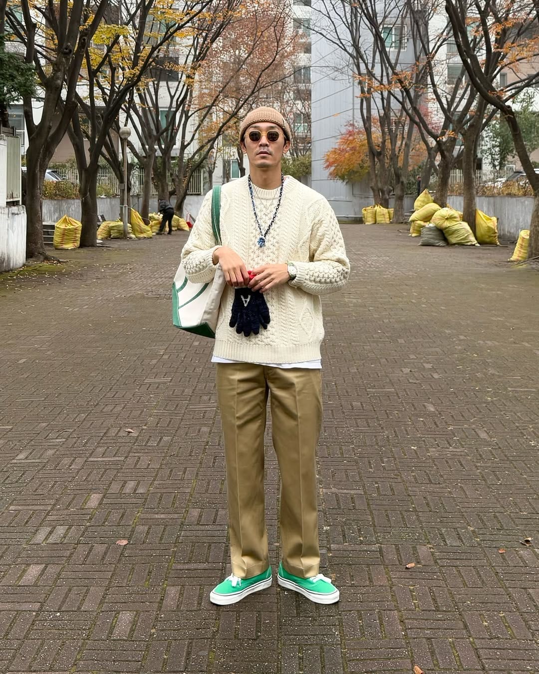 stylish man wearing a tan beanie, cream-colored fisherman sweater, tan pressed khakis, and bright green sneakers