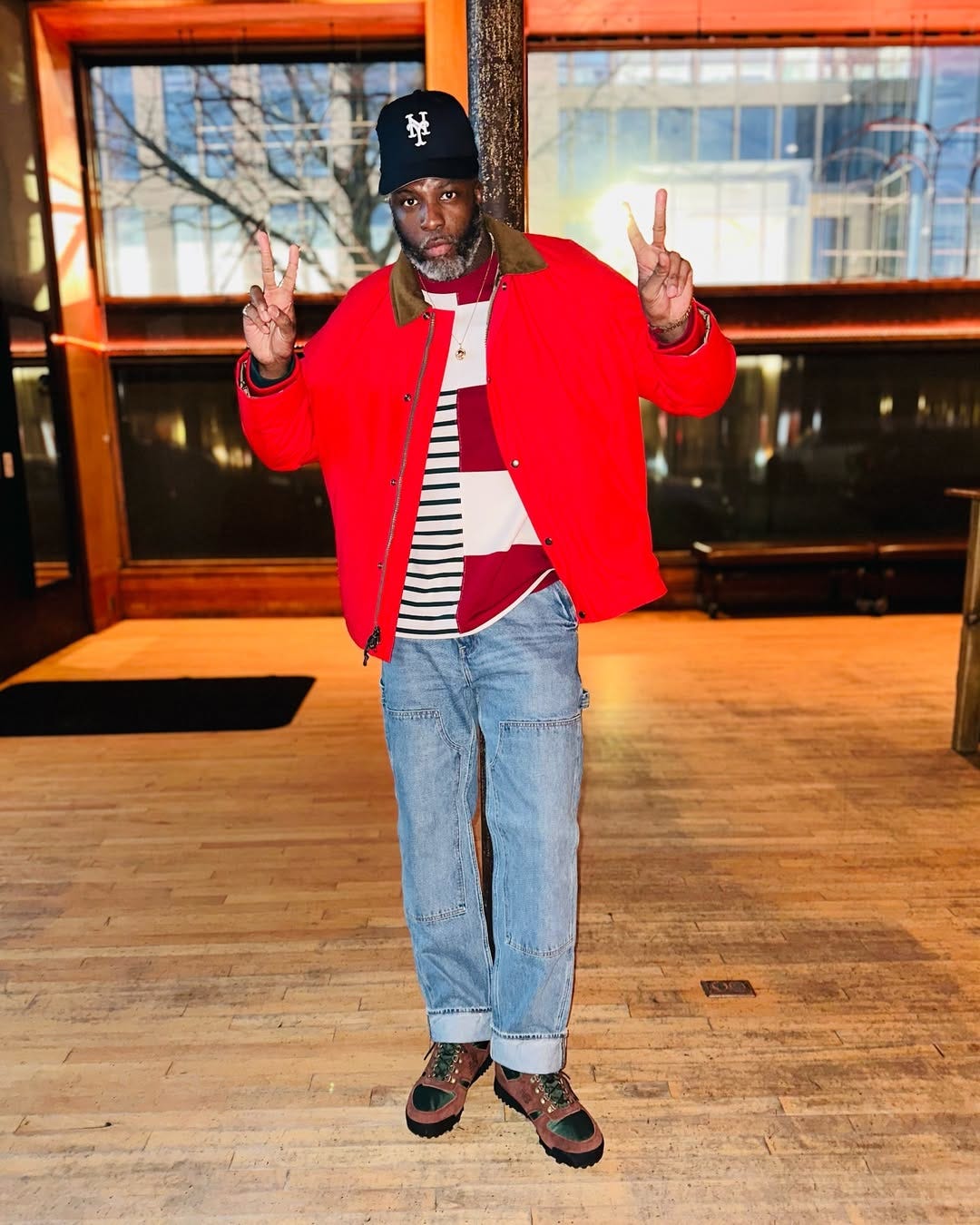 stylish man wearing a red jacket, striped maritime shirt, workwear jeans, and brown hiking boots