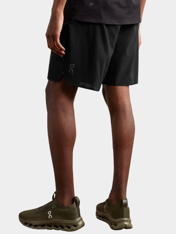 man from the waist down wearing black performance shorts and dark green sneakers