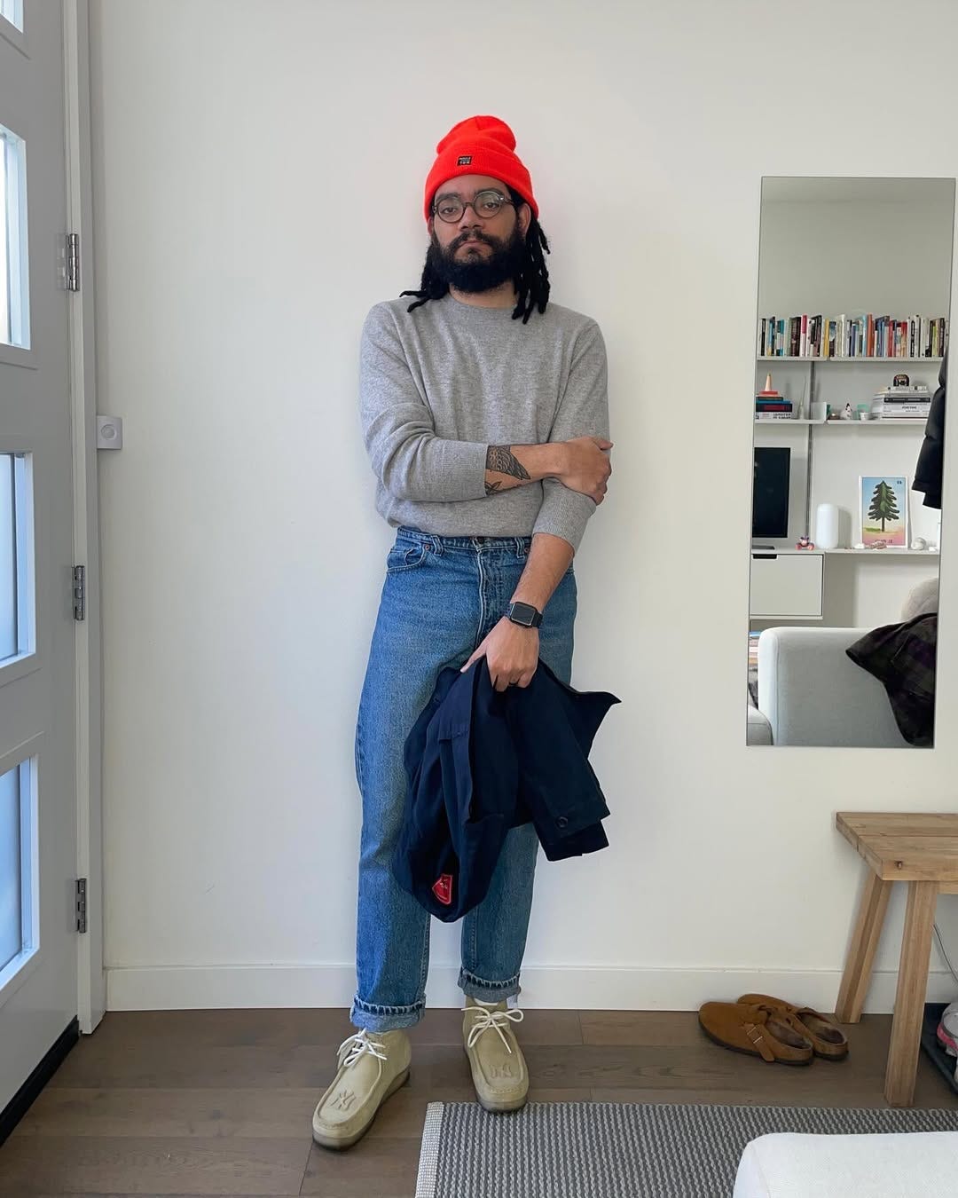 stylish man standing in a living room wearing a grey mockneck sweater with jeans and lace-up shoes