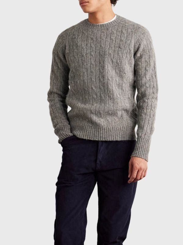 man from the neck down wearing a cable-knit wool sweater with dark pants