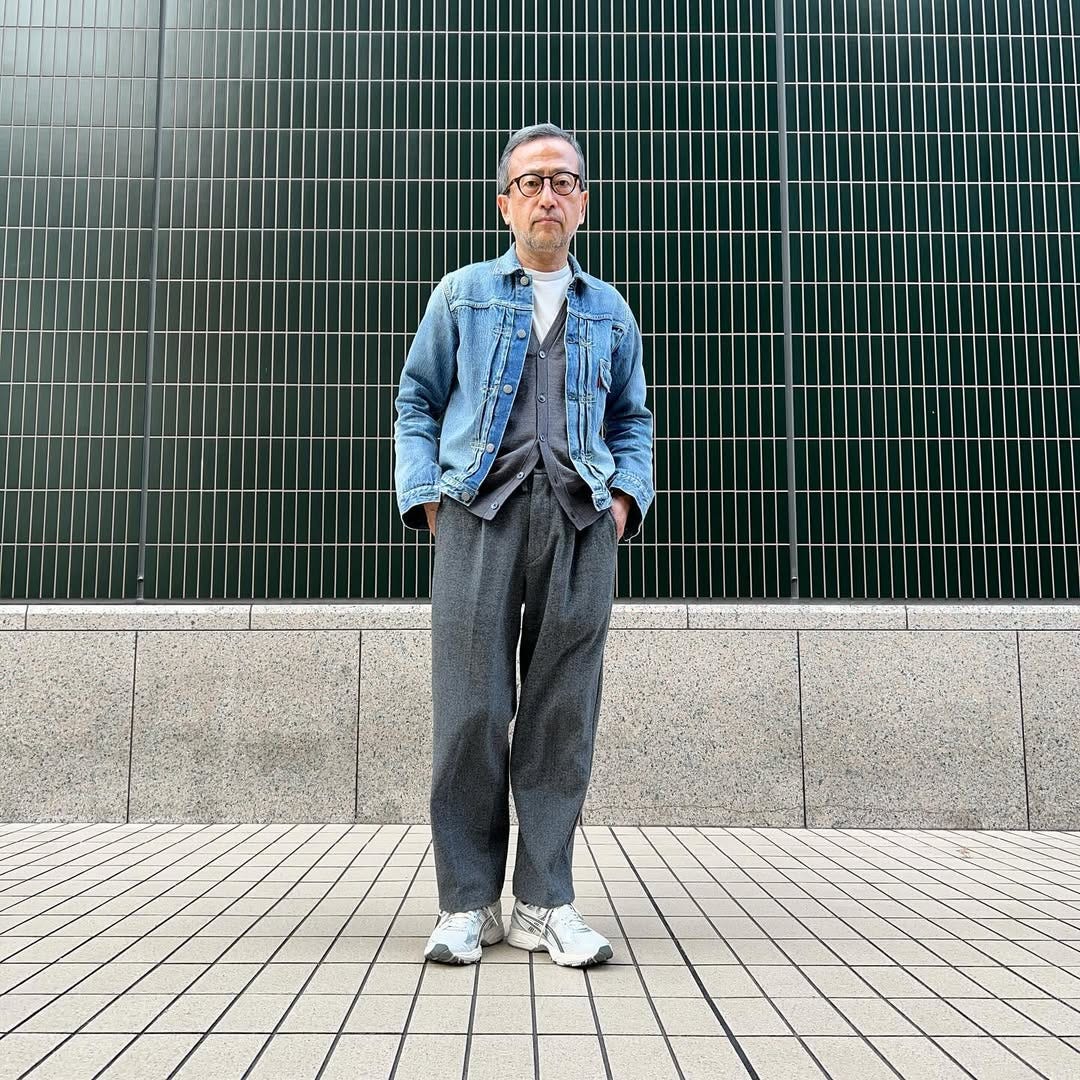 stylish man wearing a grey cardigan over a white t-shirt with a denim jacket and grey pleated dress pants