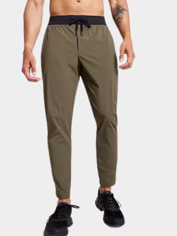 man from the waist down wearing olive green joggers with a black waistband and drawstring with black sneakers