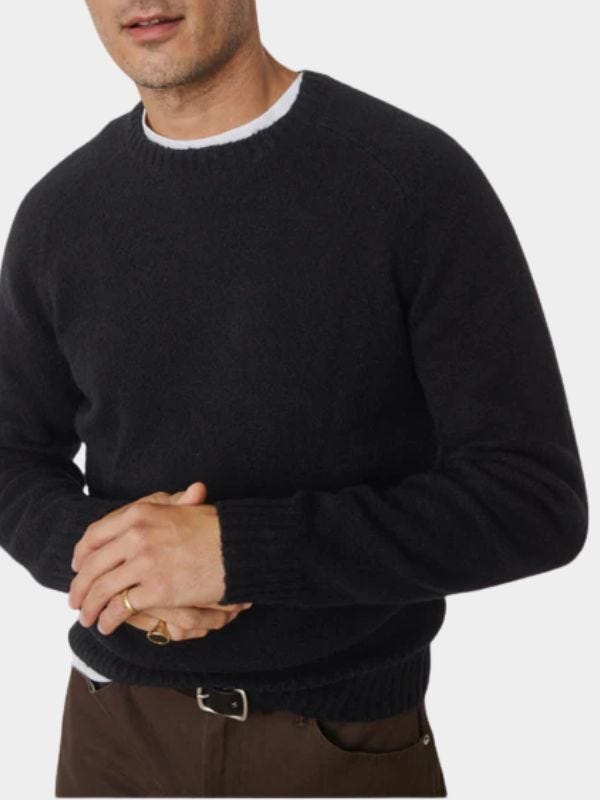 stylish man wearing a navy crewneck sweater over a white t-shirt with brown pants and a black leather belt