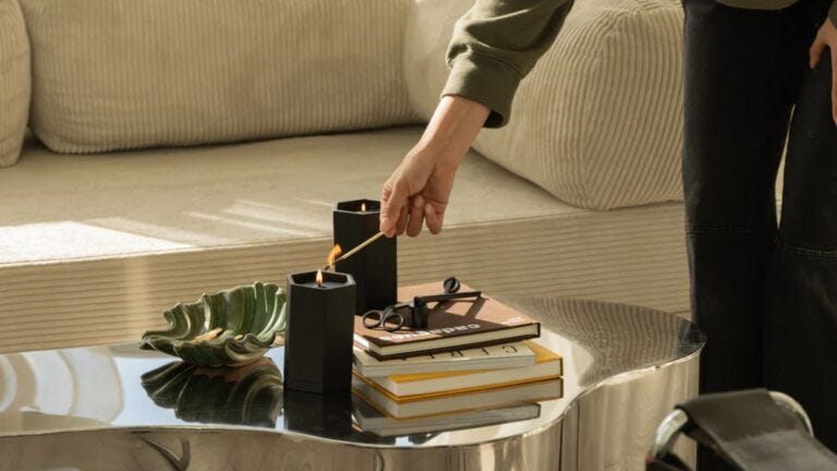 man's hand lighting a candle on a stylishly decorated coffee table in a living room in front of a cream-colored couch