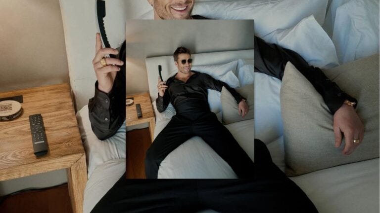 glen powell lounging on a bed in formalwear, holding a phone, wearing sunglasses, and smiling