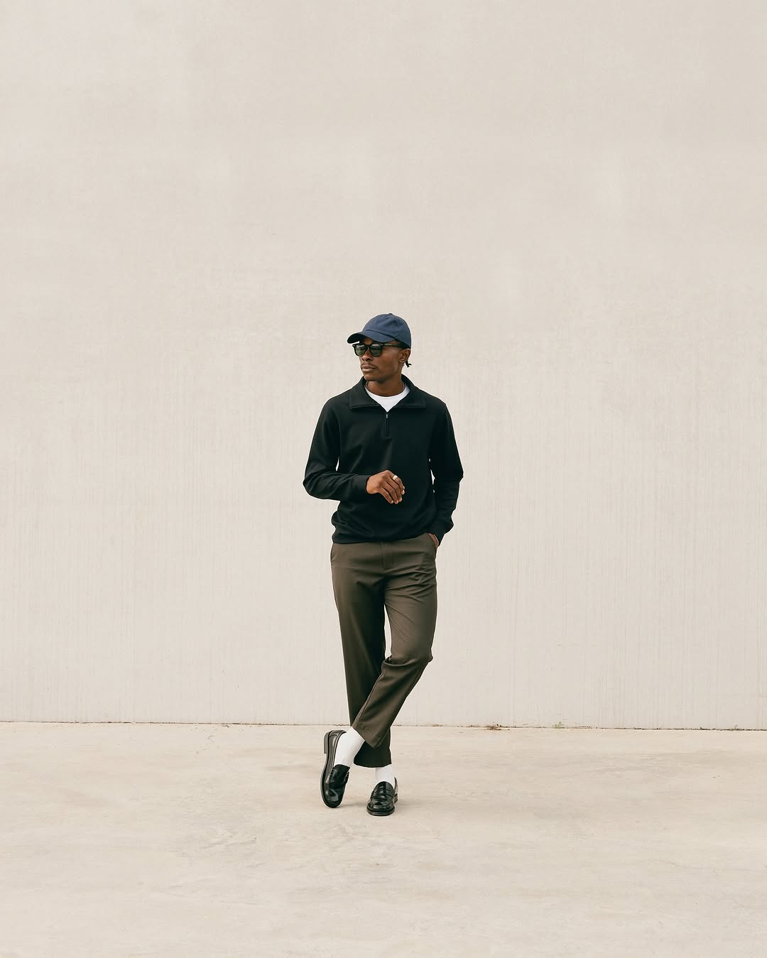 stylish man wearing a black quarter zip with olive green dress pants, white dress socks, and black penny loafers