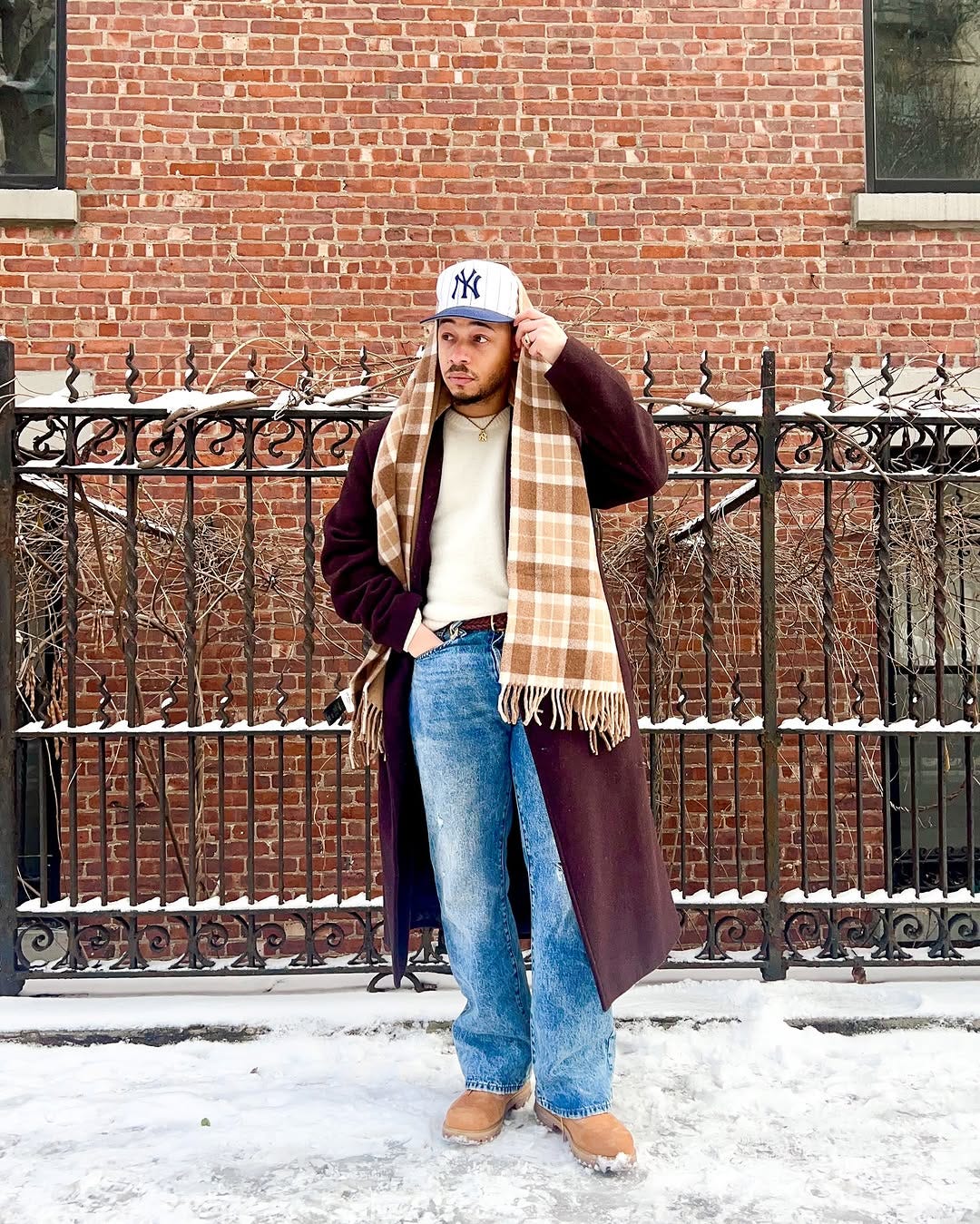 stylish man wearing a long topcoat with jeans and a scarf standing outside on a snowy street