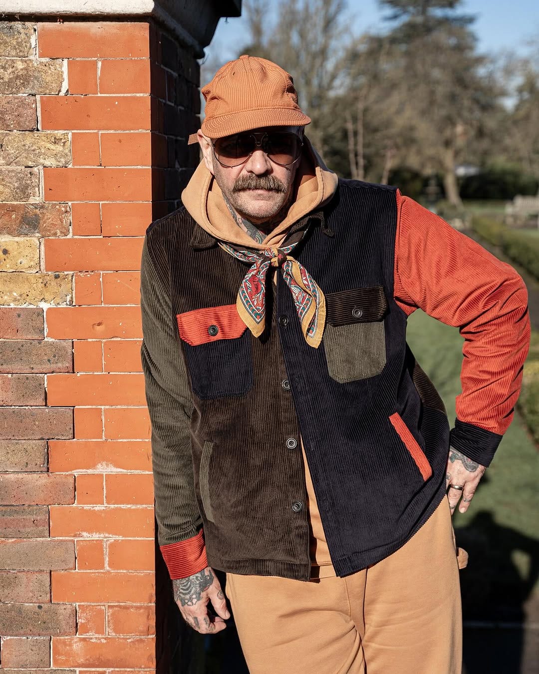 stylish man wearing a navy, orange, brown, and green corduroy shirt jacket with a paisley scarf and yellow hoodie