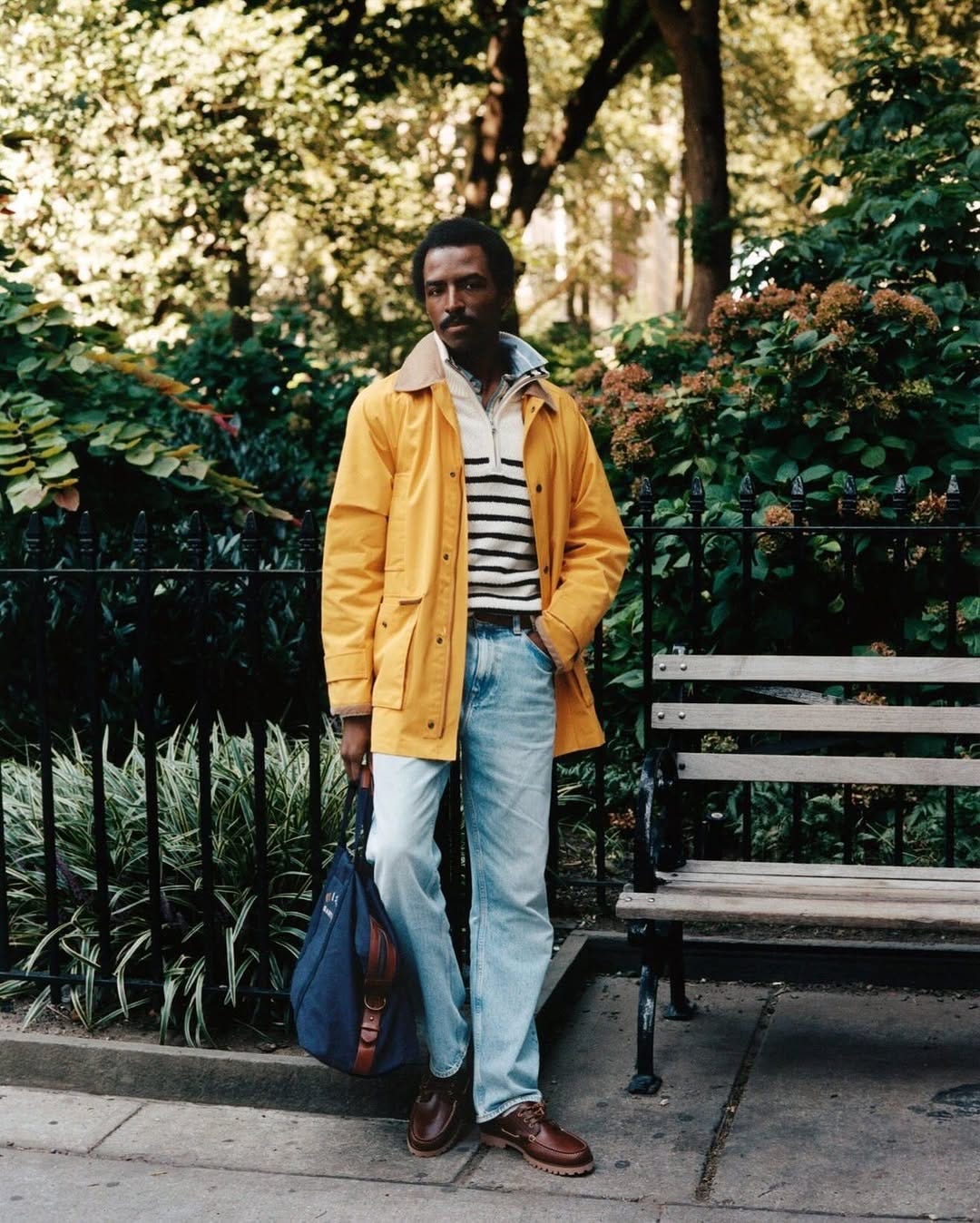 stylish man wearing a bright yellow jacket with a striped sweater and blue jeans