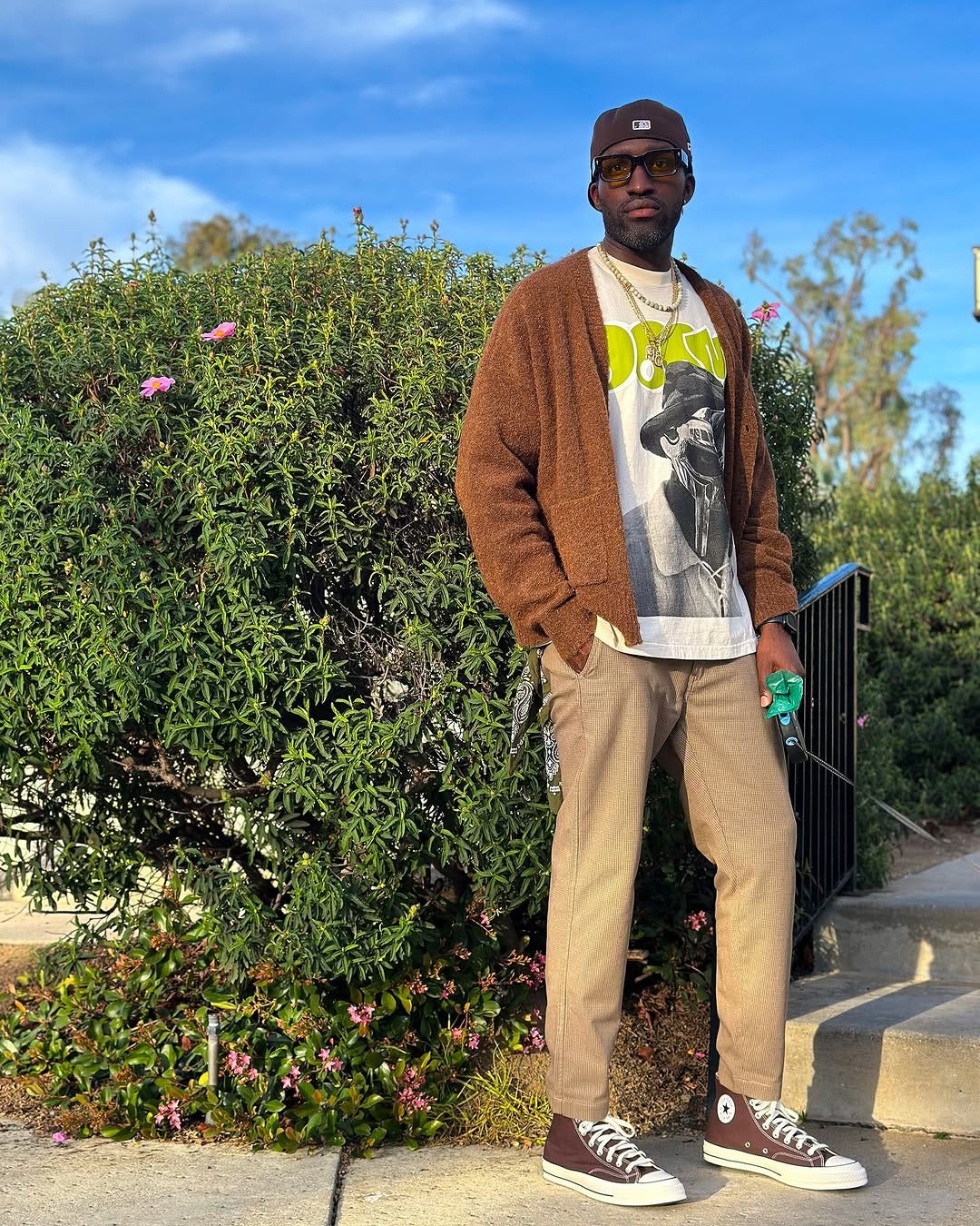 stylish man wearing a brown cardigan over a white t-shirt with lime green lettering and chinos with brown converse high-top sneakers