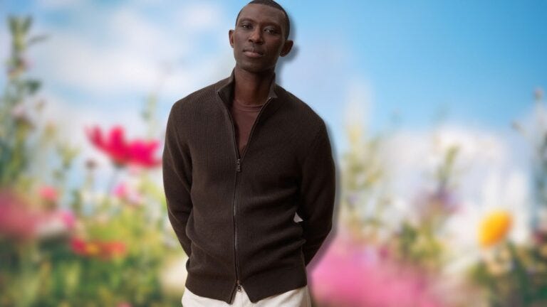 stylish man wearing a brown zip-up cardigan in front of a blurred background of spring flowers