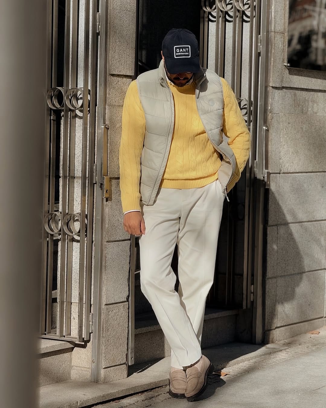 stylish man wearing a yellow cable knit sweater with a tan quilted vest and chinos