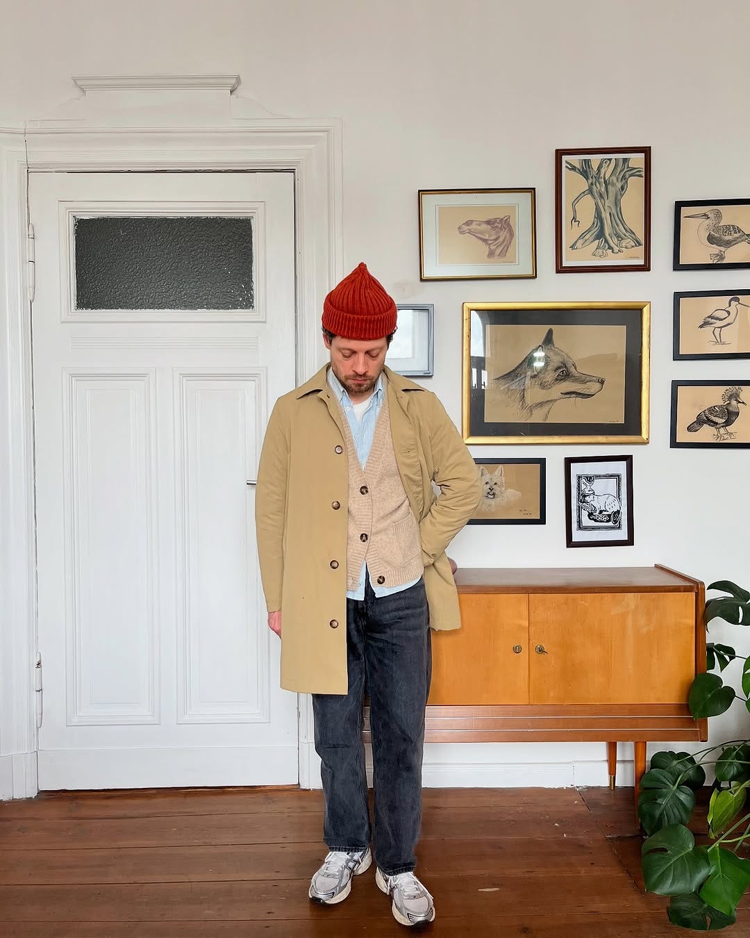 stylish man wearing a tan mac coat, light blue shirt, camel cardigan, dark pants, and asics sneakers