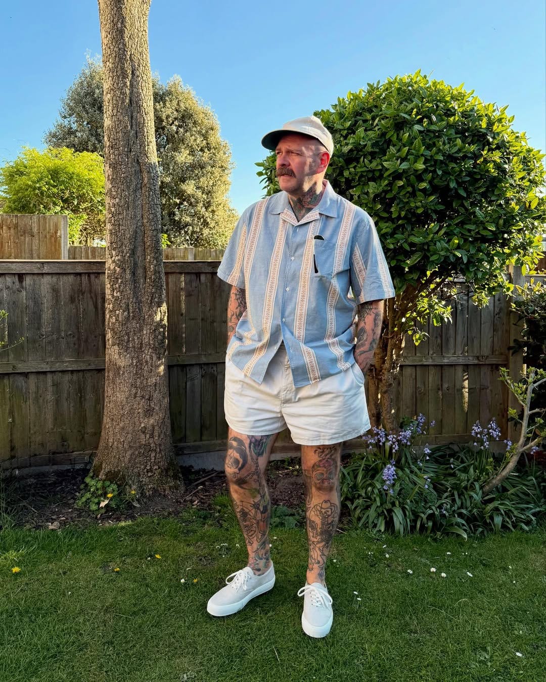 stylish man wearing a light blue camp shirt with khaki shorts and off-white sneakers